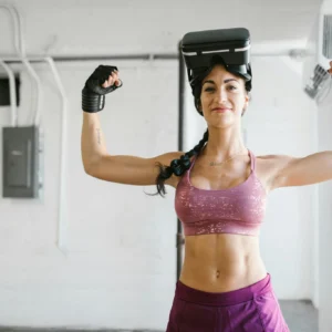 Woman flexes muscles with VR headset and gloves in gym, showcasing fitness technology.